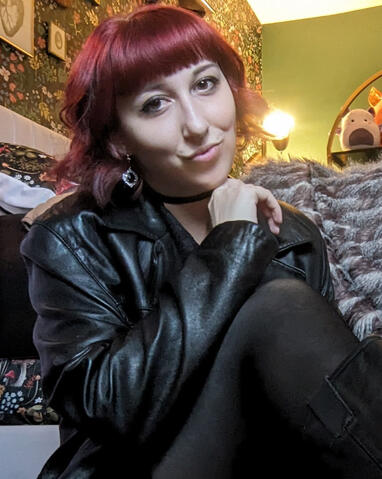 Photo of Danielle seated and smiling at the camera, her closed hand rests below her chin.